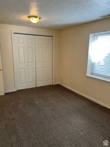 Bedroom 5 with a textured ceiling, dark colored carpet, and a closet