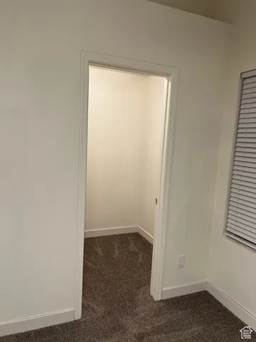 Walk in closet in Master bedroom with dark carpet and baseboards