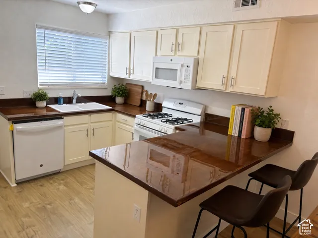 Kitchen featuring new LVP wood-finish flooring, new white appliances, cream cabinetry, new maple wood countertops, a dual basin sink, and a built-in breakfast bar