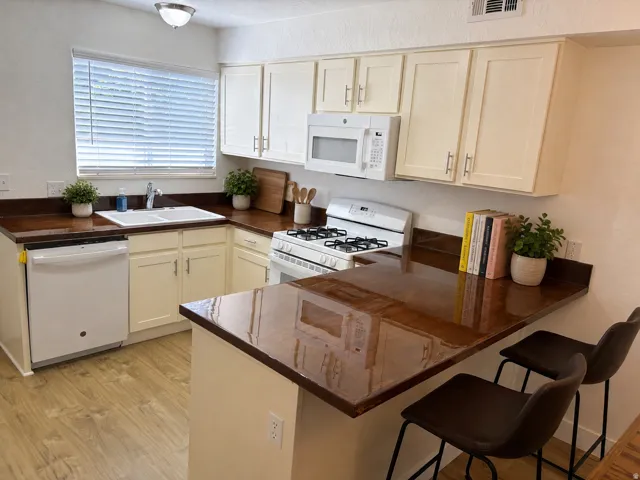 Kitchen featuring new LVP wood-finish flooring, new white appliances, cream cabinetry, new maple wood countertops, a dual basin sink, and a built-in breakfast bar