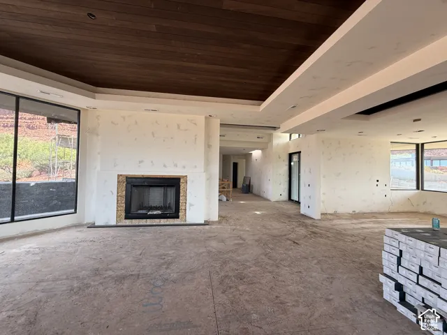 Open-concept interior featuring a recessed wood-paneled ceiling, integrated multi-tier soffit lighting, a floor-to-ceiling fireplace with a square metal hearth, and expansive picture windows