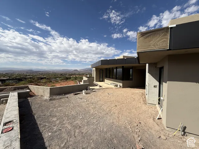 Contemporary exterior featuring smooth stucco siding, black metal fascia trim, expansive floor-to-ceiling windows, and a raised concrete terrace overlooking desert landscape