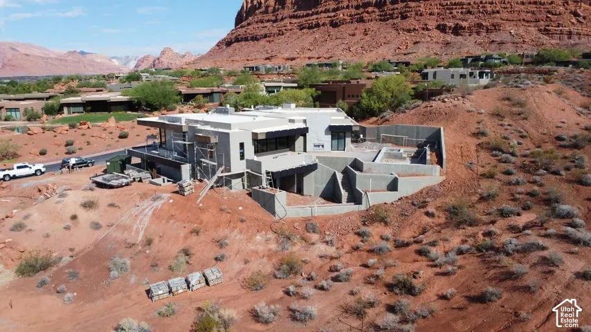 Contemporary residence featuring flat roof architecture, stucco exterior finish, expansive multi-level terraced retaining walls, and desert landscape surroundings set against a prominent red rock mountain backdrop