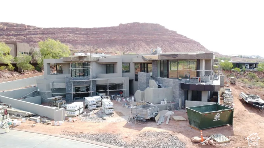 Contemporary multi-level exterior featuring stucco siding, stone veneer accents, expansive floor-to-ceiling windows, and a prominent red rock formation backdrop