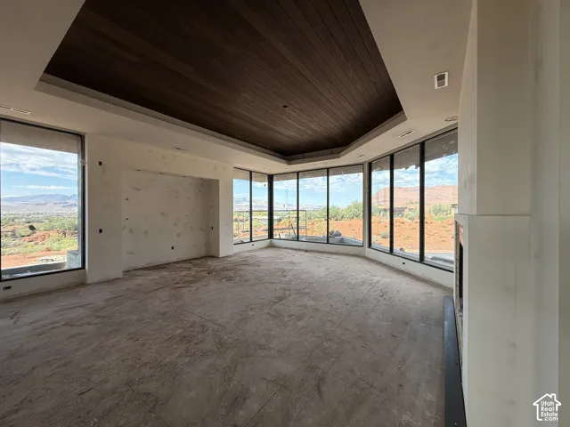 Expansive living area featuring a wood-clad tray ceiling, floor-to-ceiling windows, mountain scenery, and a built-in fireplace