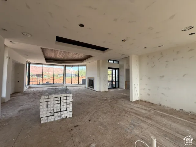Open-concept interior featuring floor-to-ceiling windows, a recessed tray ceiling with wood-plank inlay, a built-in fireplace, and expansive mountain scenery