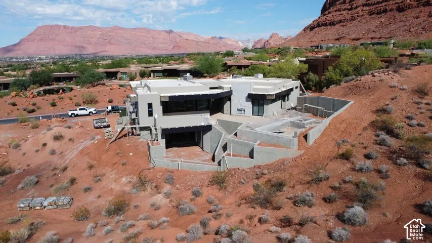 Contemporary multi-level residence featuring a flat roofline, stucco exterior, integrated garage, concrete retaining walls, and mountain scenery