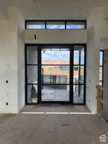 Floor-to-ceiling metal-framed glass entry door system with matching side lites and transom window, accented by exterior stone cladding and a mountainous backdrop