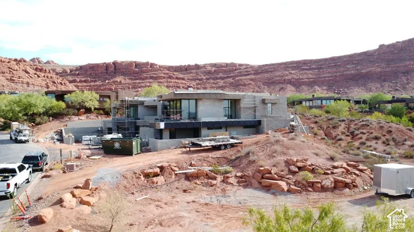 Multi-level contemporary structure featuring concrete exterior finishes, expansive glass windows, and a flat roofline, positioned against a prominent red rock mountain backdrop