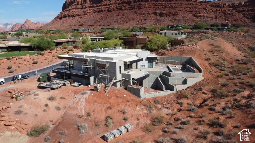Modern architectural structure featuring flat rooflines, expansive concrete walls, multi-level terraced foundations, and red rock mountain surroundings