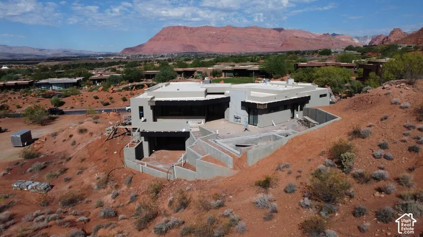 Contemporary residence featuring a flat roofline, stucco exterior, multi-level concrete retaining walls, and a recessed lower-level garage, set against a prominent mountain backdrop