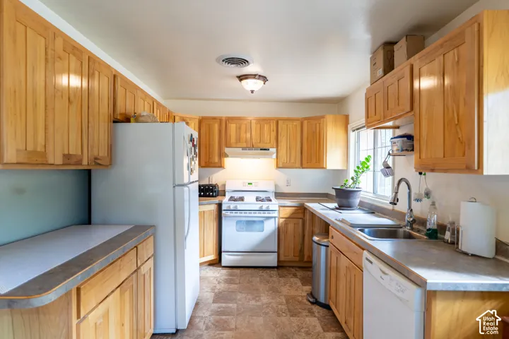 Kitchen featuring white appliances, stone finish floors, and under cabinet range hood