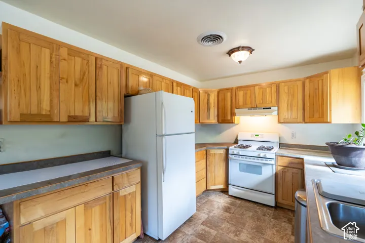 Kitchen with white appliances, stone finish flooring, under cabinet range hood, and brown cabinets