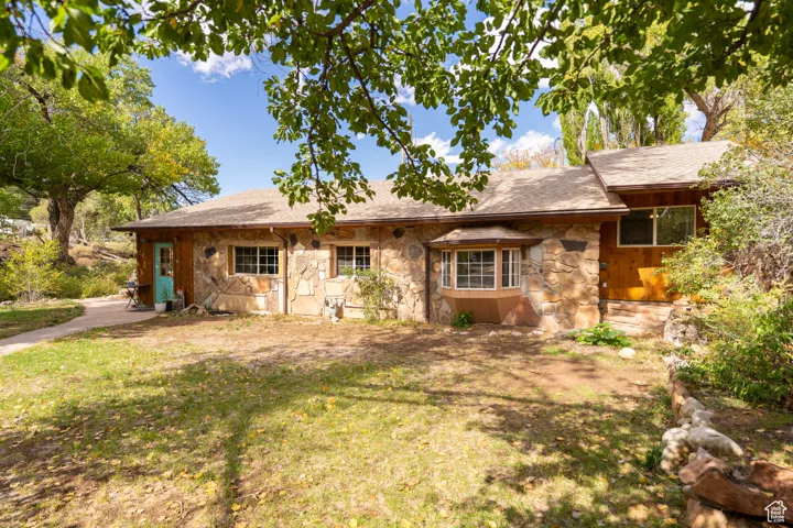 View of front of home featuring stone siding, a shingled roof, and a front yard