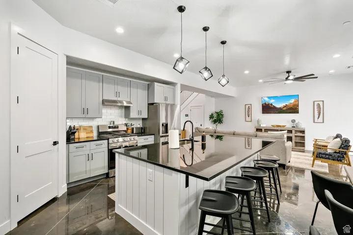 Kitchen with backsplash, stainless steel appliances, open floor plan, a kitchen bar, and ceiling fan
