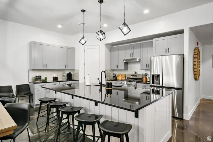 Kitchen with appliances with stainless steel finishes, a large island, decorative backsplash, a kitchen bar, and recessed lighting