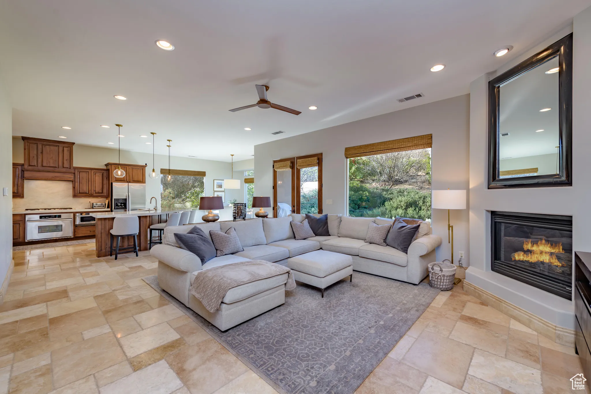 Living room featuring recessed lighting, healthy amount of natural light, a ceiling fan, a glass covered fireplace, and stone tile flooring