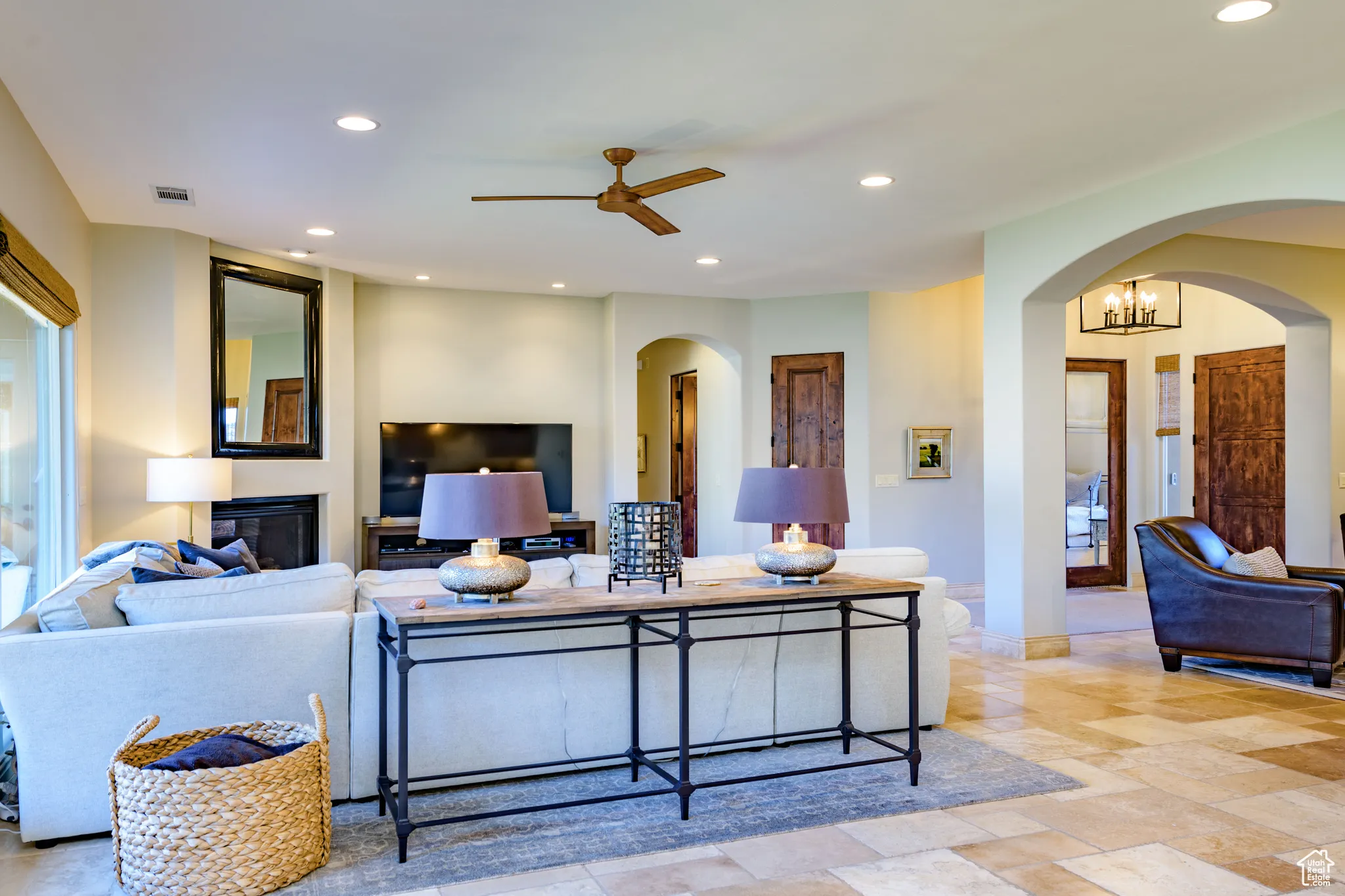 Living room with arched walkways, recessed lighting, a glass covered fireplace, ceiling fan, and stone tile flooring