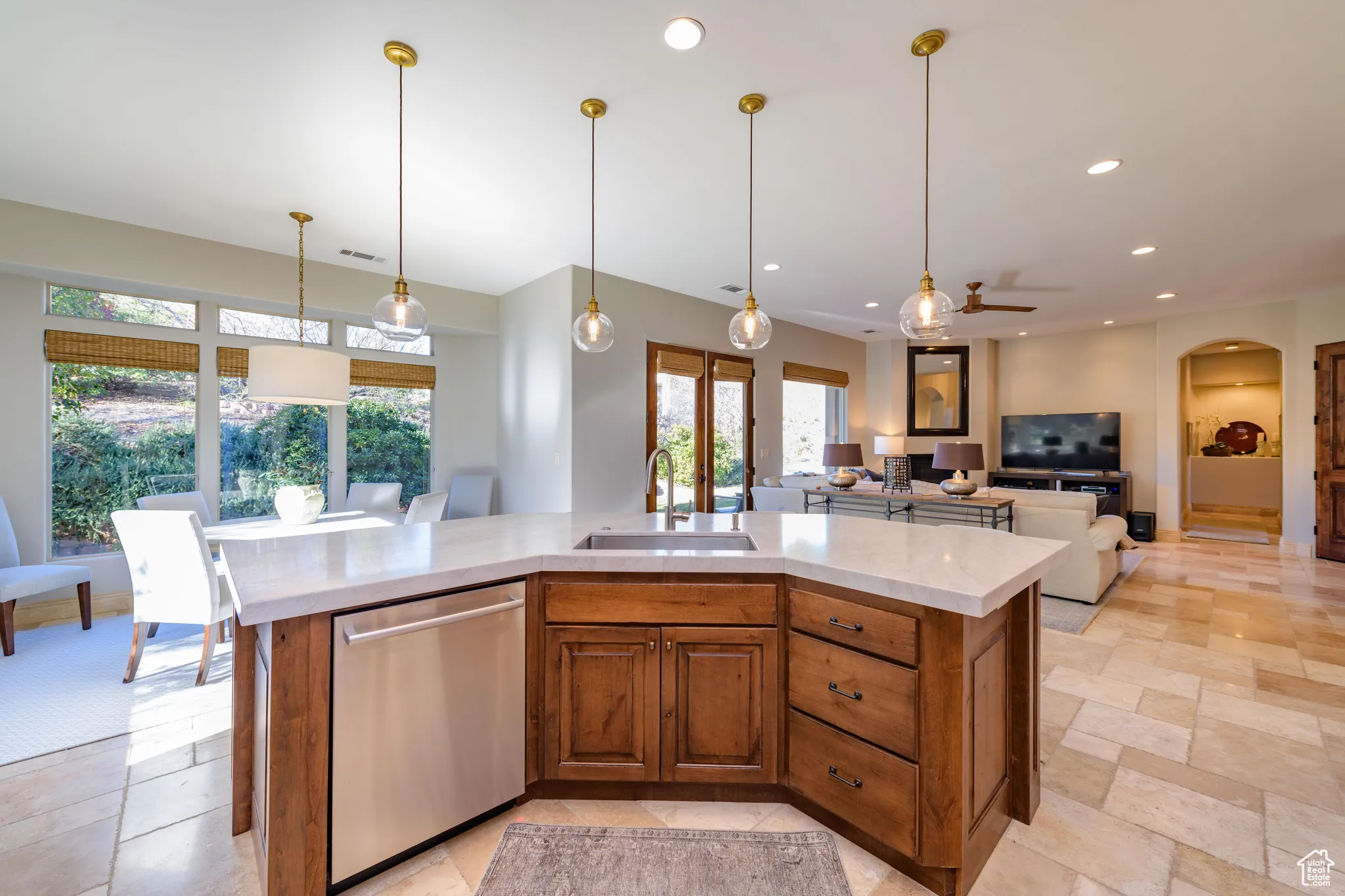 Kitchen featuring brown cabinetry, hanging light fixtures, stainless steel dishwasher, a kitchen island with sink, and recessed lighting