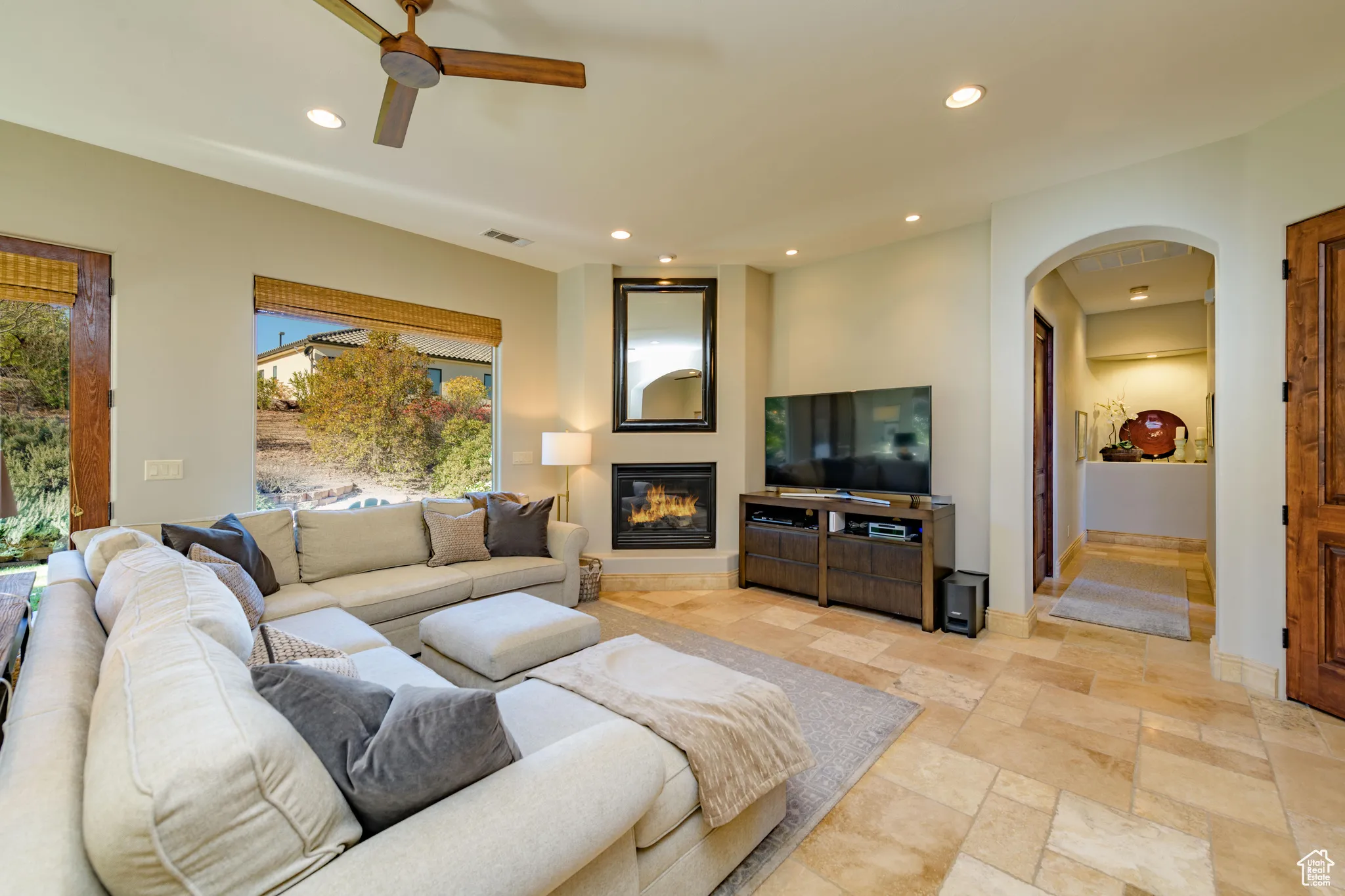 Living area featuring recessed lighting, arched walkways, a glass covered fireplace, stone tile floors, and ceiling fan