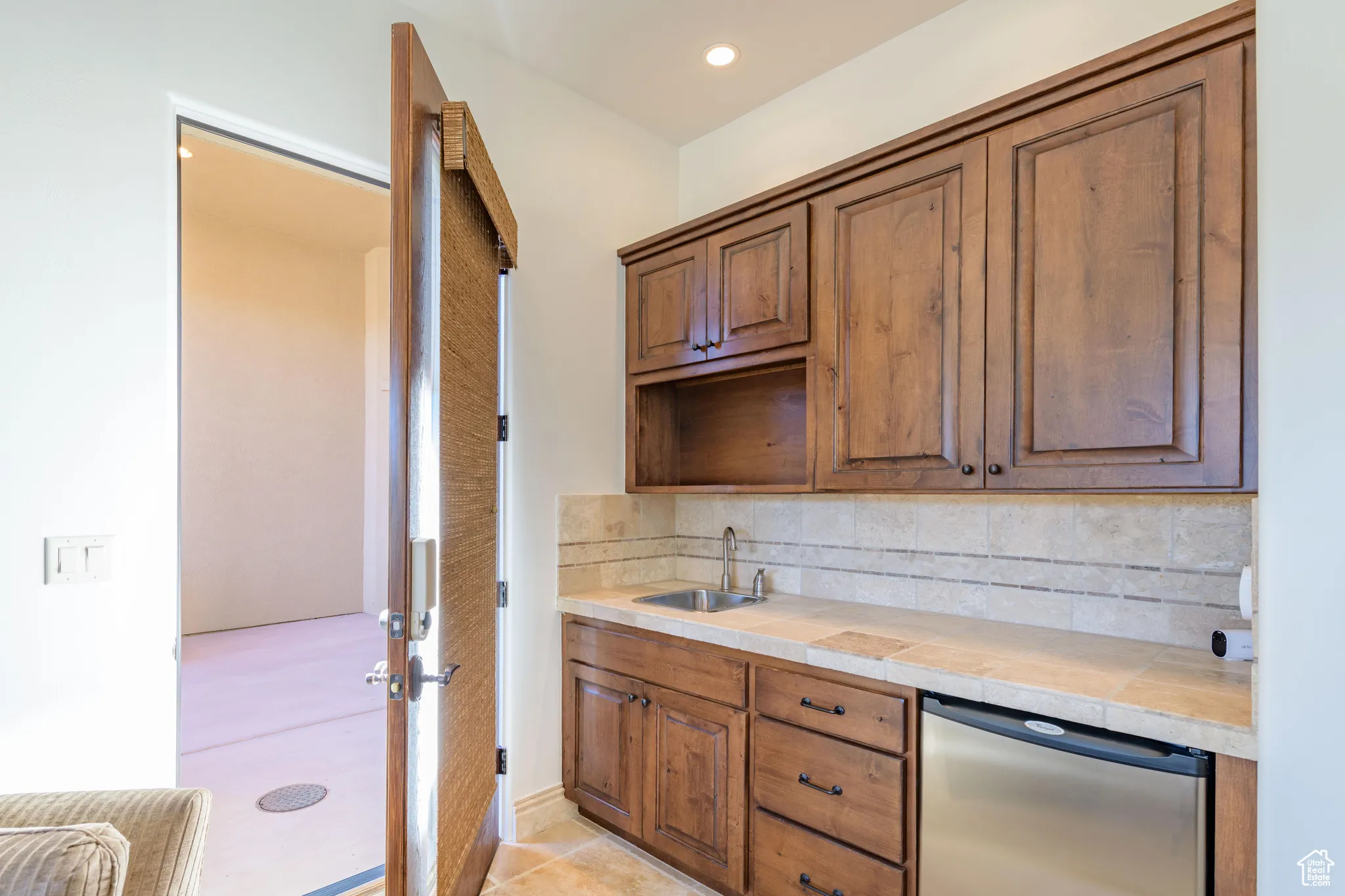 Kitchen with tasteful backsplash, stainless steel dishwasher, brown cabinetry, light tile patterned floors, and recessed lighting