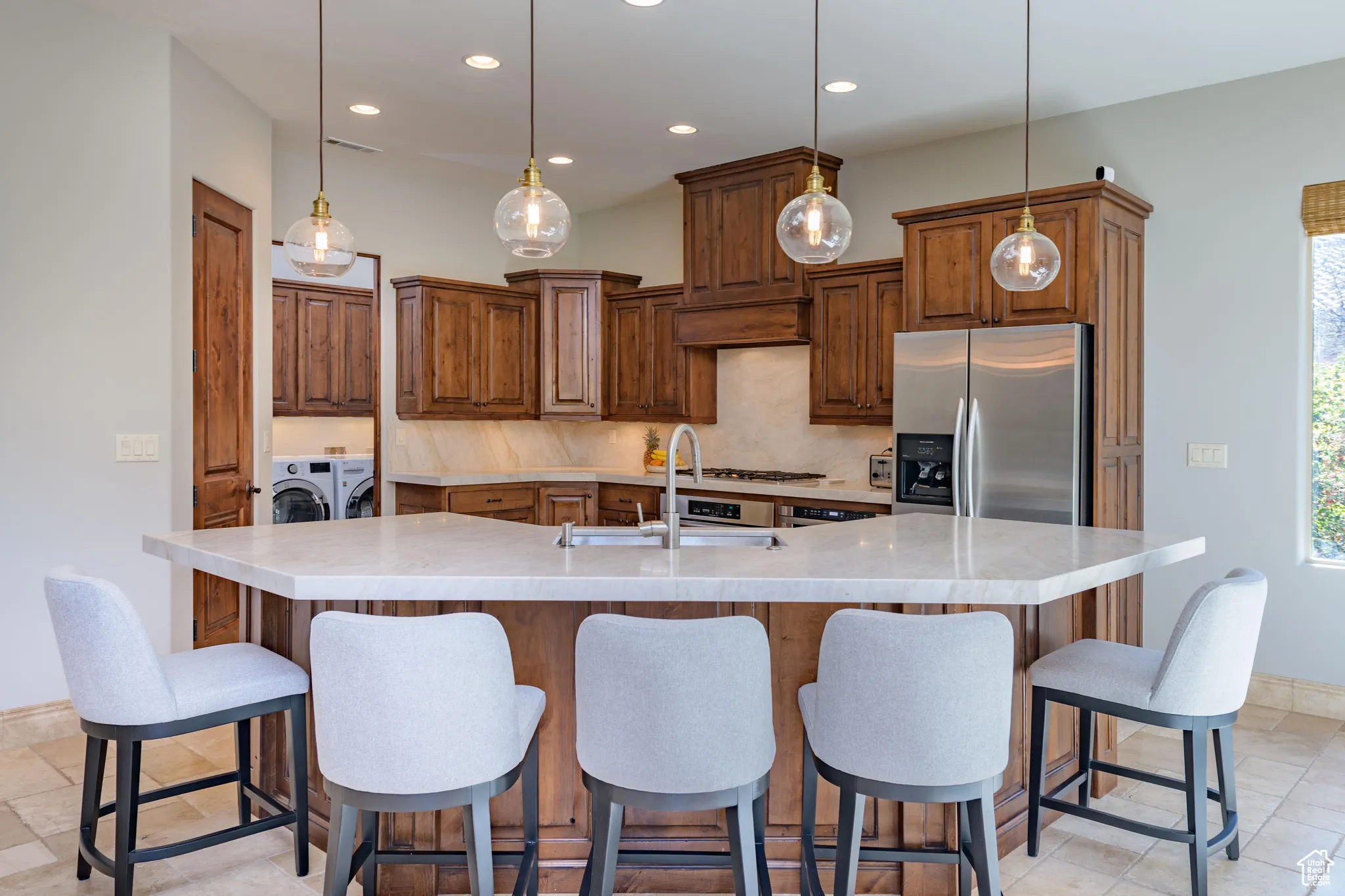 Kitchen featuring stainless steel fridge, brown cabinets, tasteful backsplash, a breakfast bar area, and recessed lighting