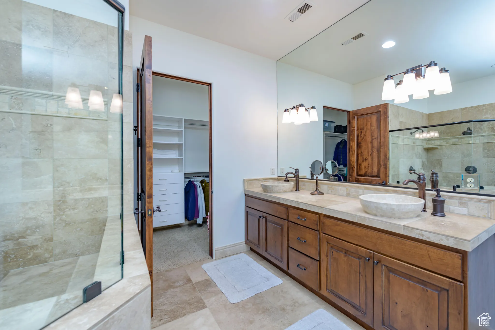 Full bathroom with a spacious closet, a shower stall, double vanity, and light tile patterned floors