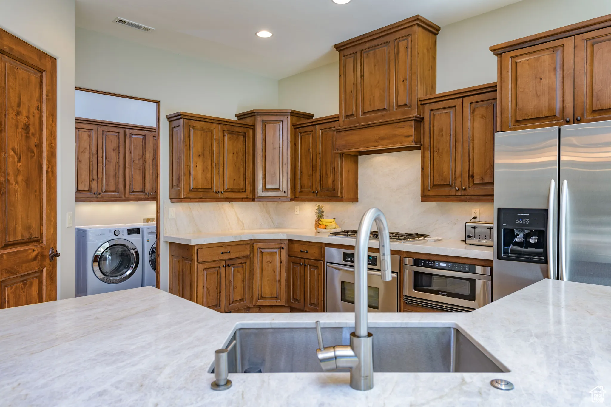 Kitchen featuring appliances with stainless steel finishes, brown cabinets, backsplash, recessed lighting, and washing machine and clothes dryer