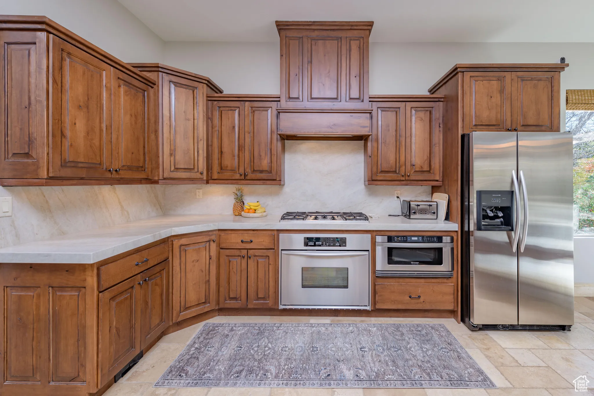 Kitchen with stainless steel appliances, brown cabinets, backsplash, and stone tile flooring