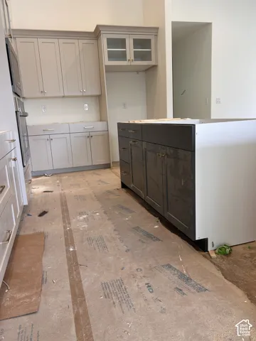 Kitchen featuring shaker-style cabinetry with crown molding, glass-front upper cabinet, central island, and built-in wall oven