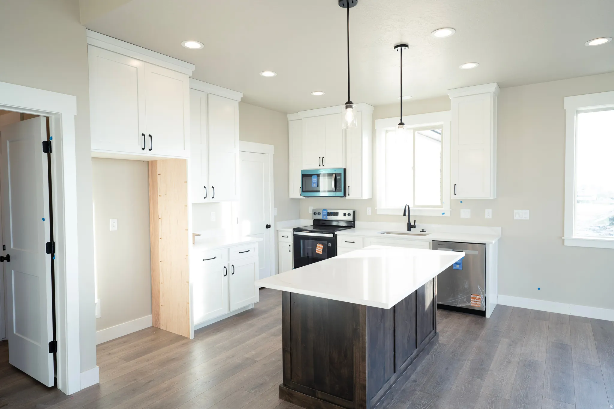 Kitchen with stainless steel appliances, decorative light fixtures, a kitchen island, white cabinets, and dark wood-style flooring
