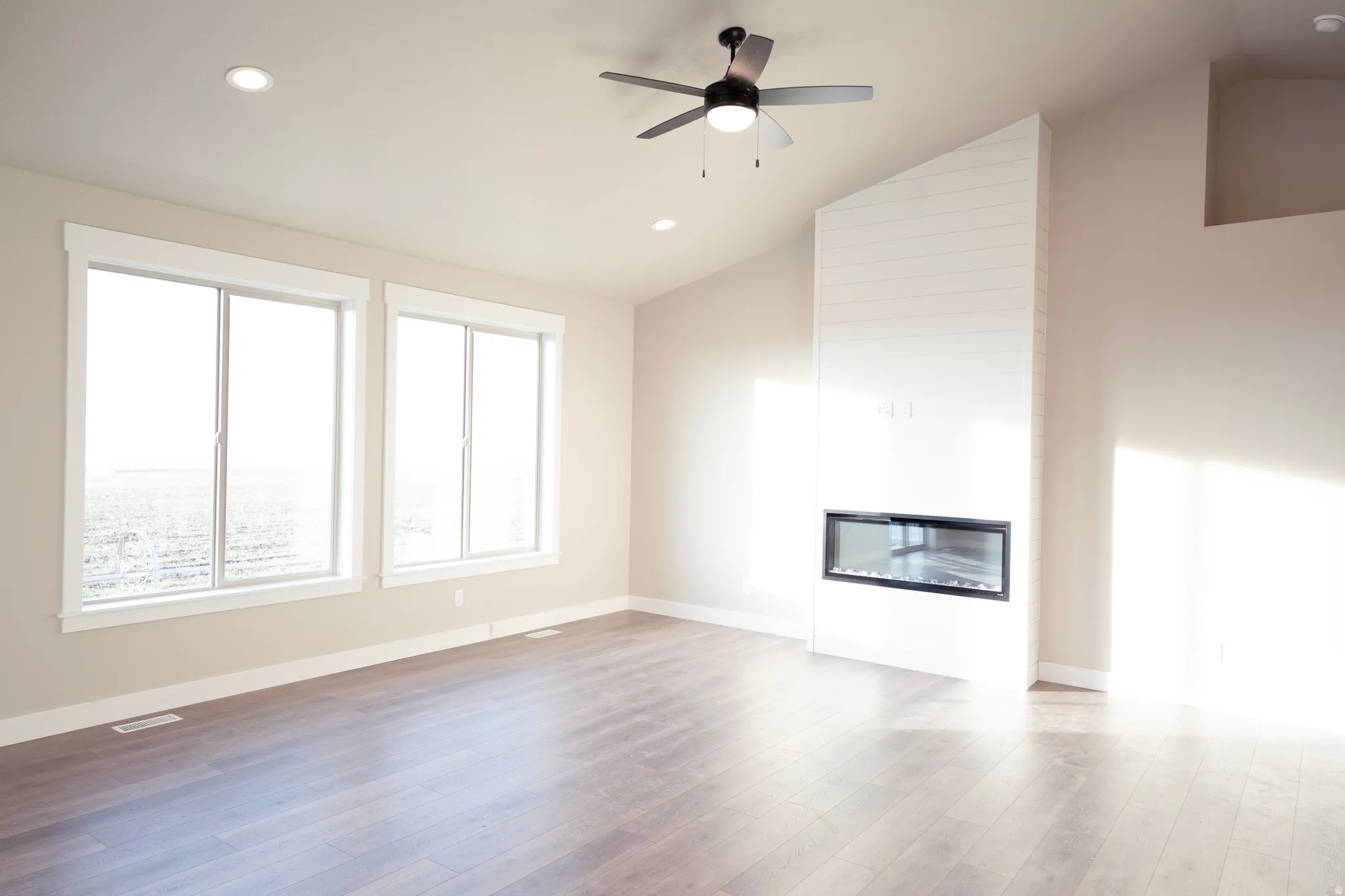Unfurnished living room with a fireplace, lofted ceiling, light wood-type flooring, a ceiling fan, and recessed lighting