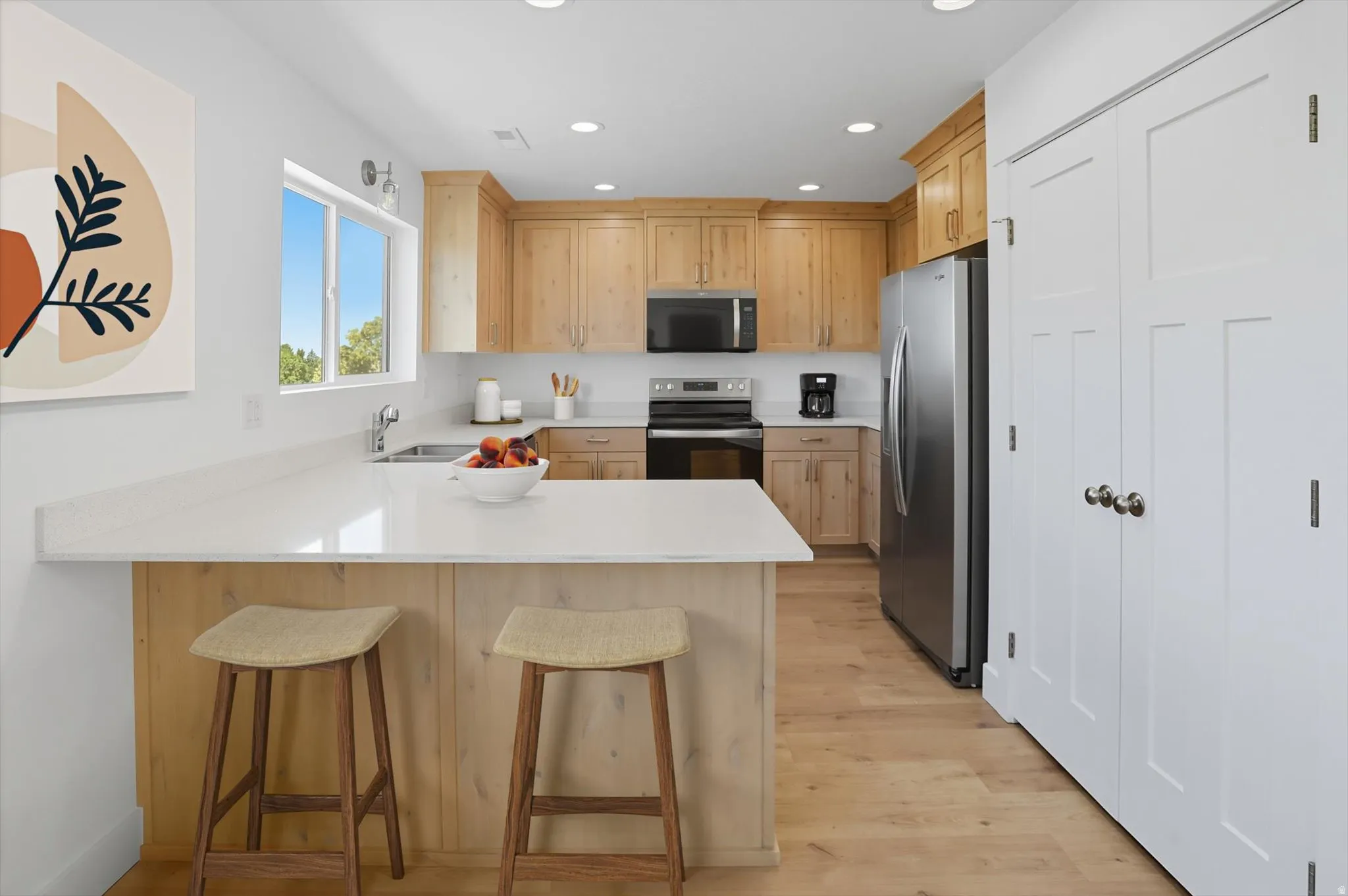 Kitchen with a peninsula, stainless steel appliances, a kitchen bar, light wood-style flooring, and light wood finish cabinetry