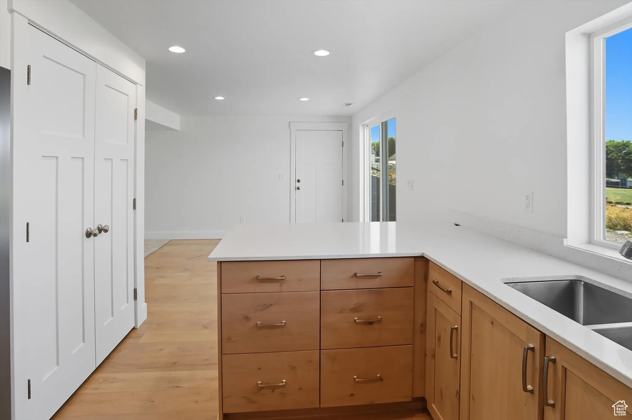 Kitchen featuring recessed lighting, a peninsula, light wood-style floors, light stone counters, and brown cabinets