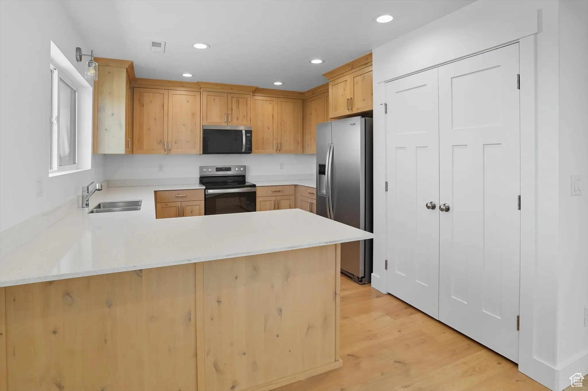 Kitchen with a peninsula, light brown cabinets, appliances with stainless steel finishes, light wood-type flooring, and recessed lighting