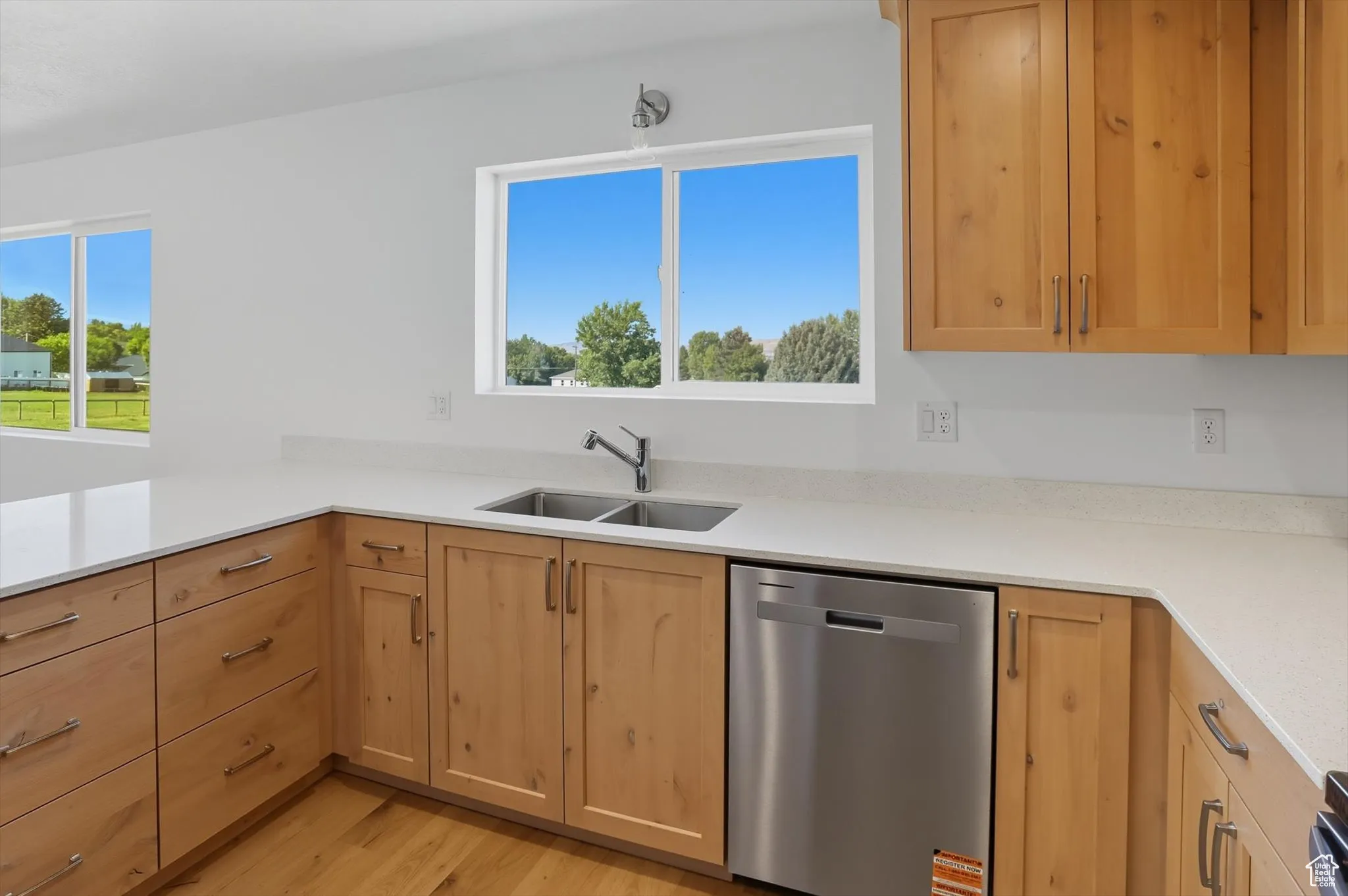 Kitchen with dishwasher, light stone counters, light brown cabinetry, and light wood-style flooring