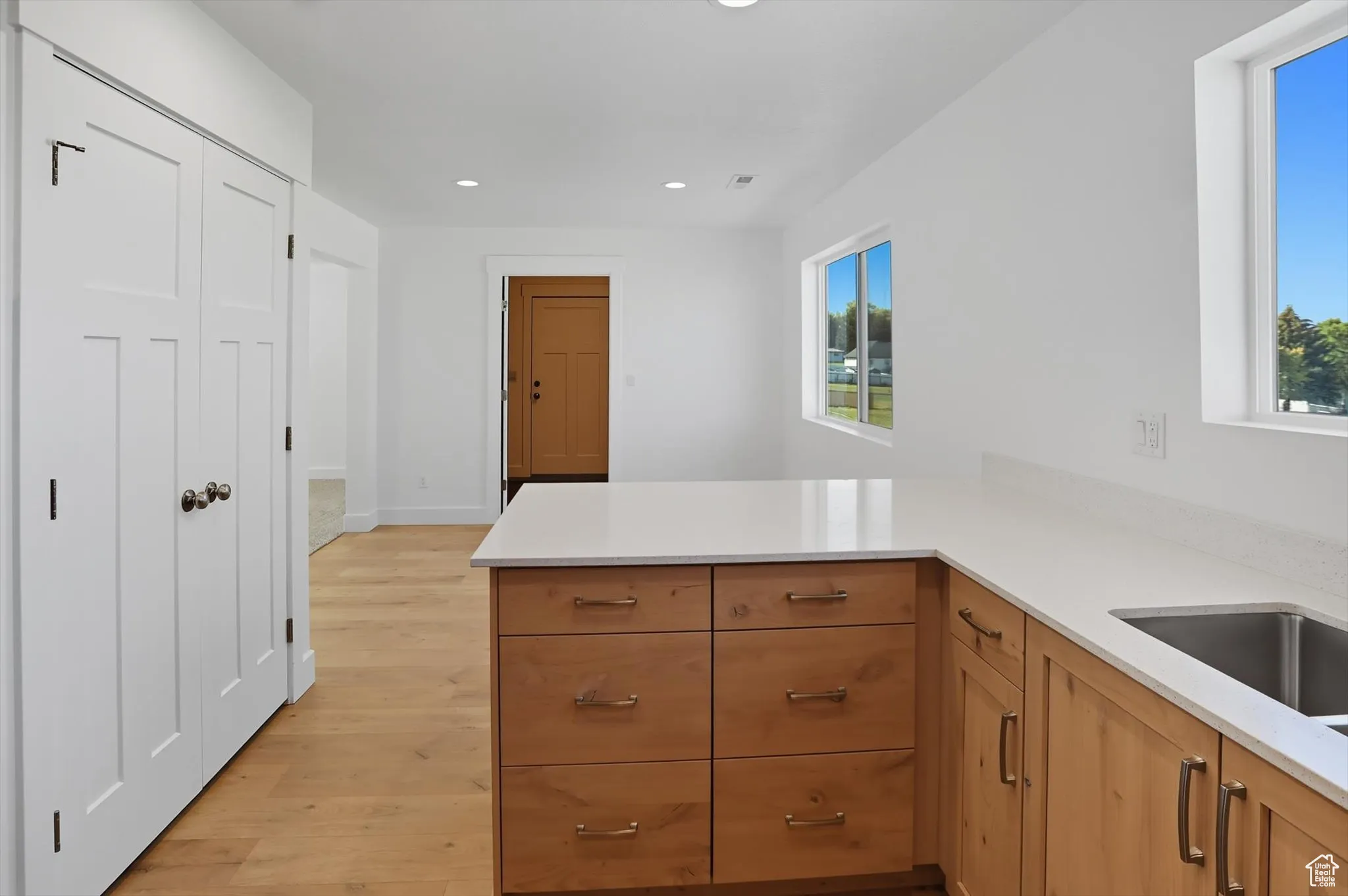 Kitchen with recessed lighting, light wood finished floors, a peninsula, light stone counters, and brown cabinetry