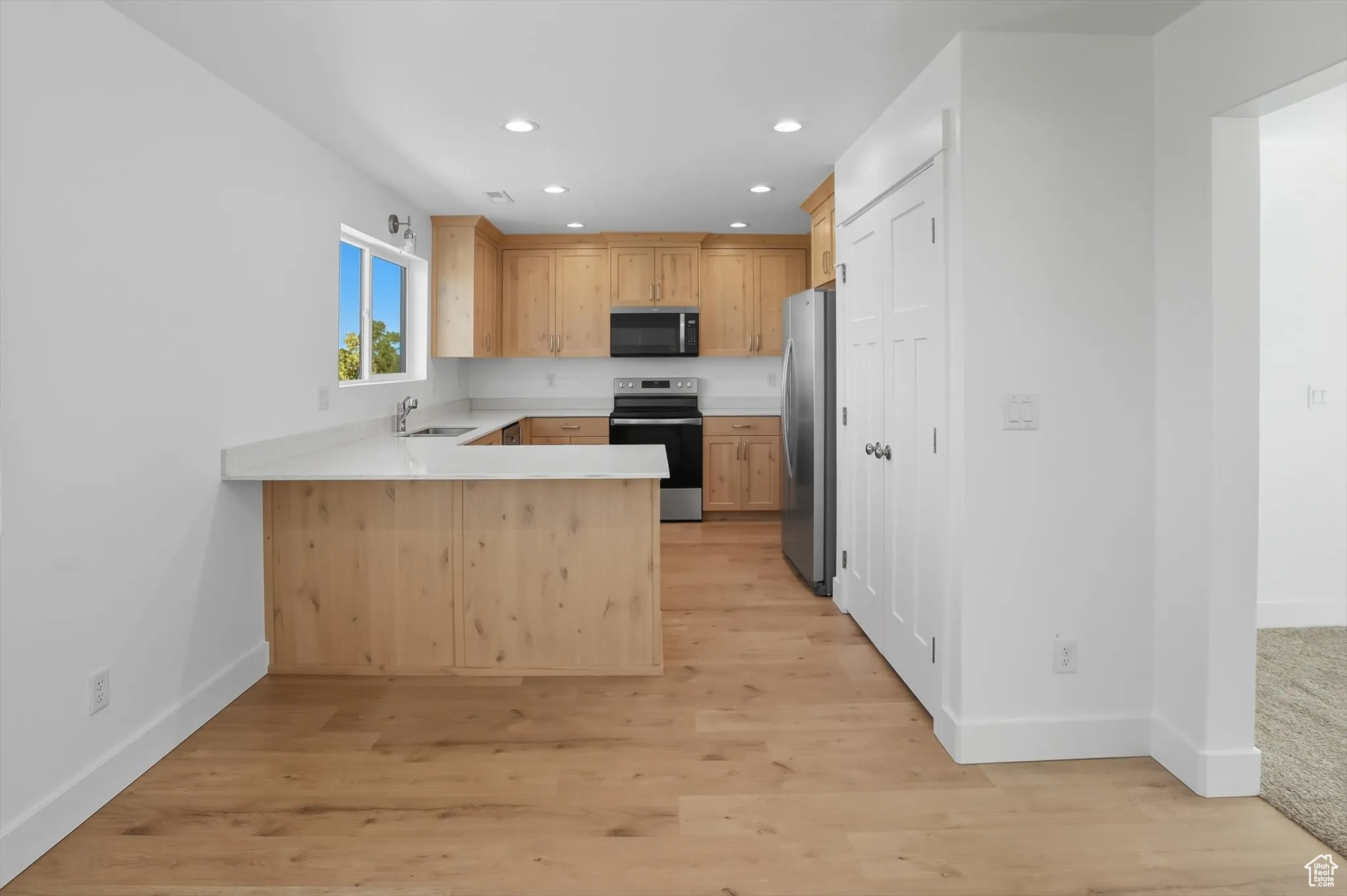 Kitchen with a peninsula, light brown cabinetry, appliances with stainless steel finishes, recessed lighting, and light wood finished floors