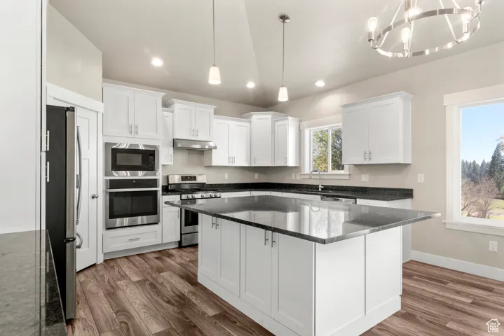 Kitchen with stainless steel appliances, white cabinetry, a kitchen island, decorative light fixtures, and dark stone counters