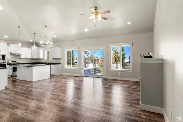Unfurnished living room featuring healthy amount of natural light, a chandelier, a ceiling fan, dark wood-style floors, and recessed lighting