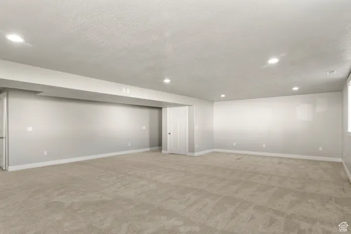 Finished below grade area featuring light colored carpet, a textured ceiling, and recessed lighting