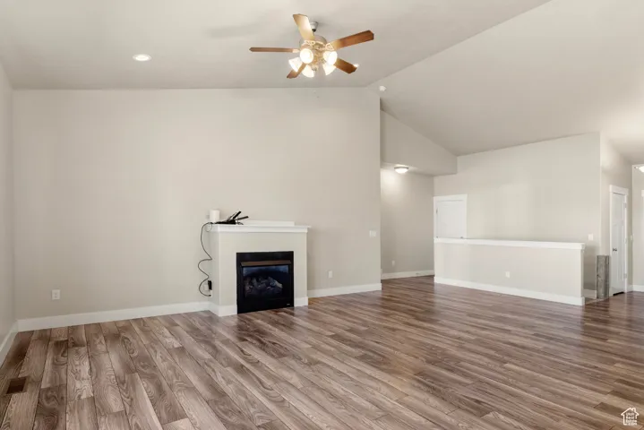 Unfurnished living room featuring a glass covered fireplace, wood finished floors, ceiling fan, recessed lighting, and high vaulted ceiling
