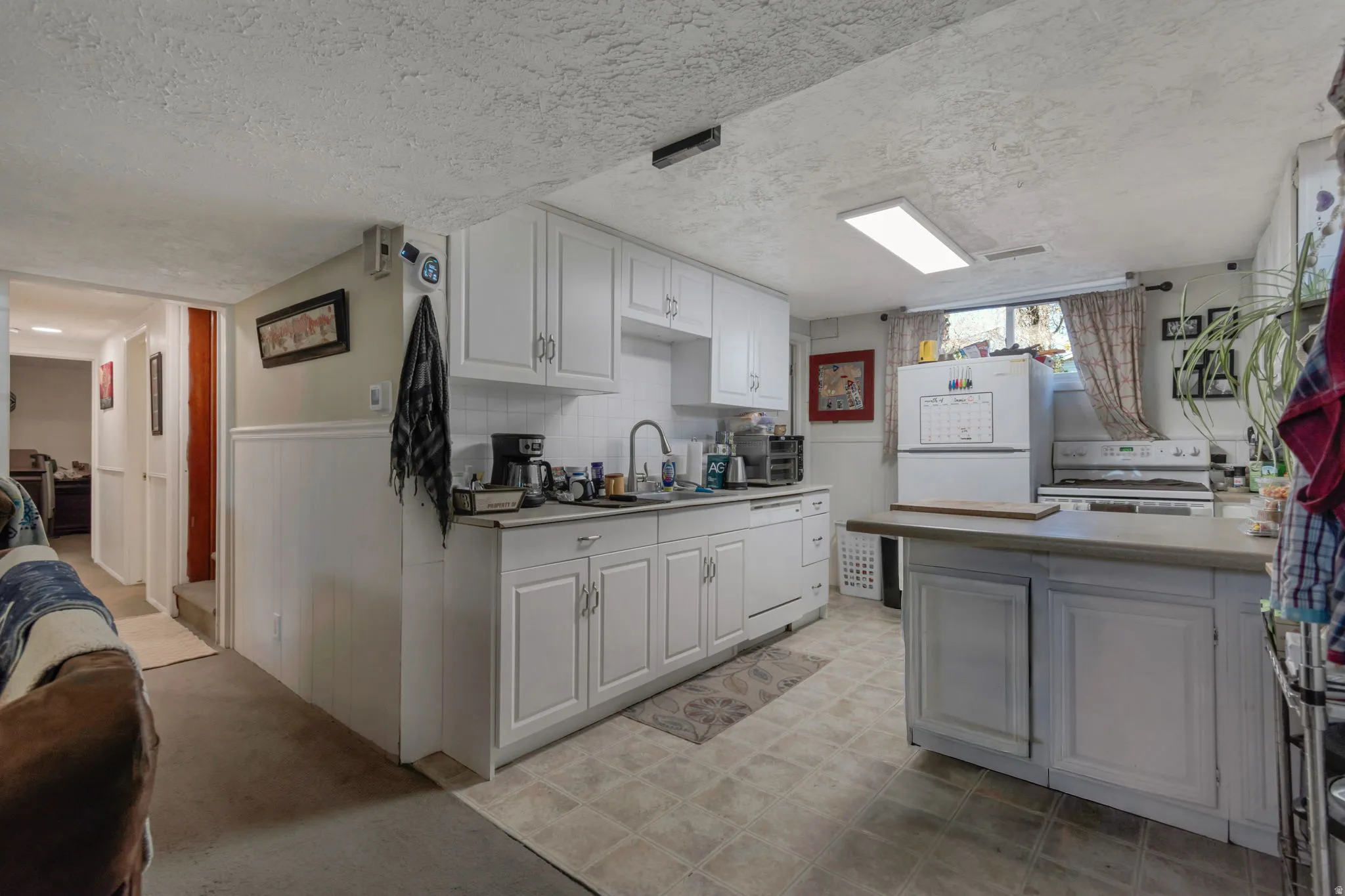 Basement Kitchen featuring light countertops, white cabinetry, white appliances, a peninsula, and a textured ceiling