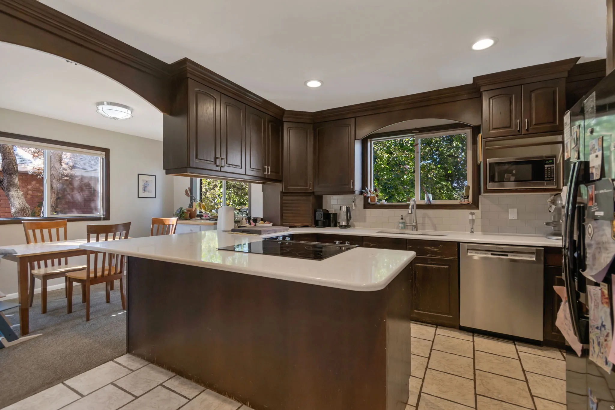 Kitchen featuring black appliances, backsplash, dark brown cabinetry, light tile patterned floors, and a peninsula