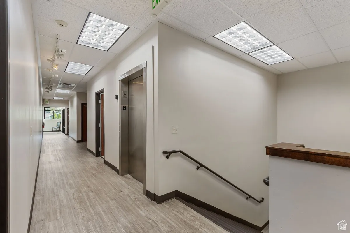 Hall with a drop ceiling, an upstairs landing, elevator, and light wood-style flooring