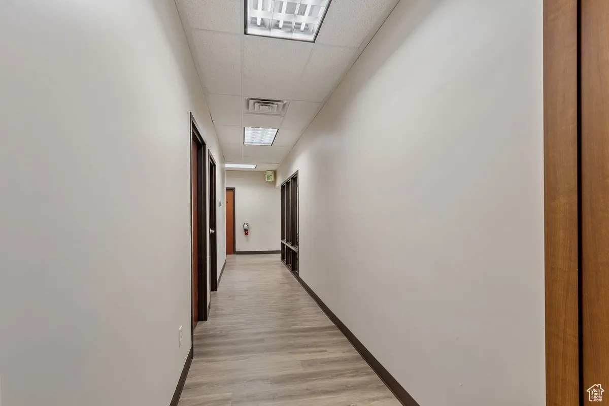 Corridor with a paneled ceiling and light wood-style flooring
