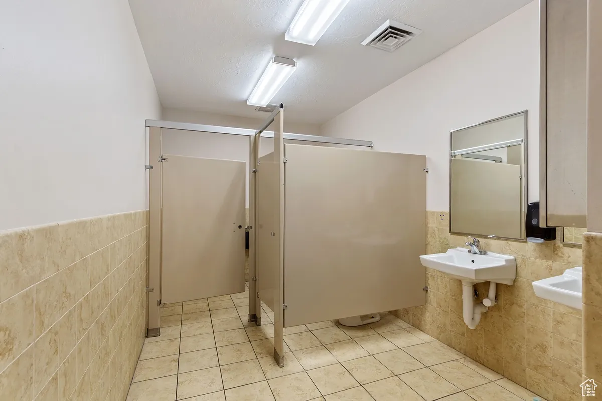 Bathroom featuring tile walls, a wainscoted wall, light tile patterned floors, and a shower stall