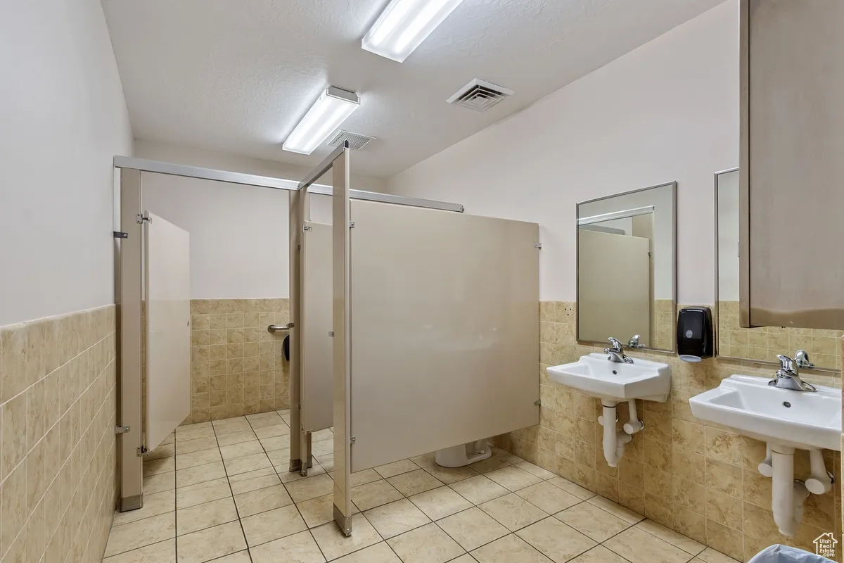 Full bath with tile walls, a stall shower, a wainscoted wall, and light tile patterned floors
