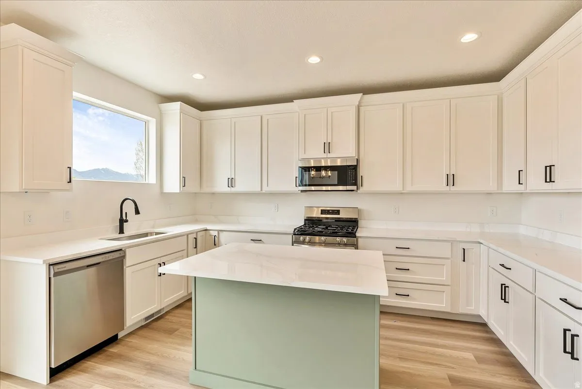 Kitchen with a center island, stainless steel appliances, light stone countertops, recessed lighting, and light wood-style floors