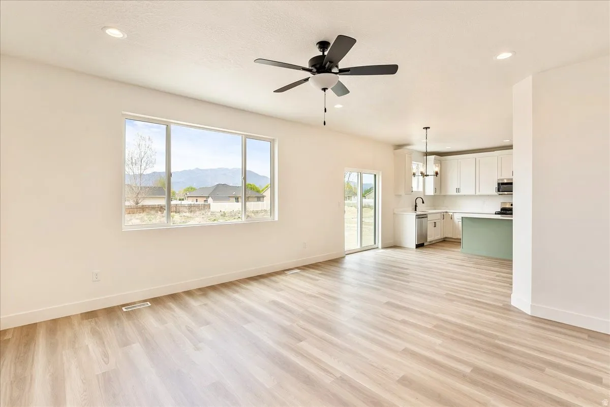 Unfurnished living room featuring a mountain view, ceiling fan, light wood-style flooring, and suspended lighting
